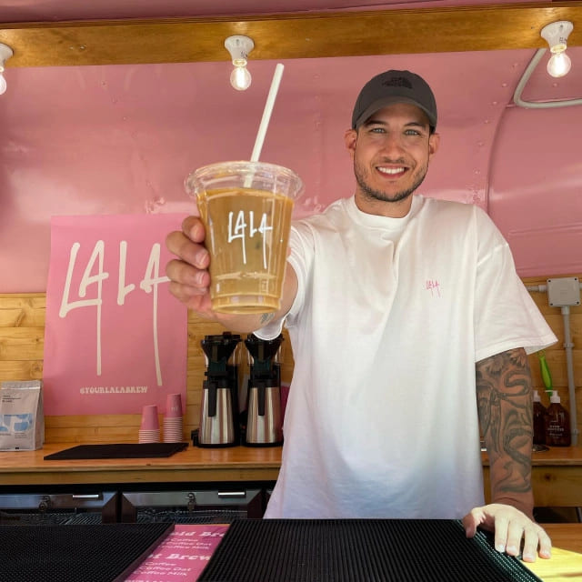 Two hands holding iced coffee drinks in branded plastic cups with Doughnut Time logo, set against a vibrant backdrop. Perfect example of branded plastic cups used for café promotions.